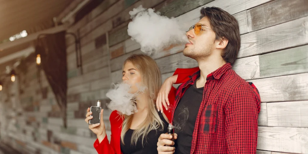 Couple enjoying vape mods outdoors against wooden wall – Vape Mods for Beginners.