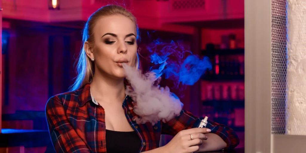 Young woman using vape mod in a lounge with colorful lights – Vape Mods for Beginners.