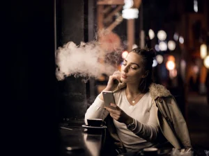 Woman using vape mod while checking phone in a café – Vape Mods for Beginners.
