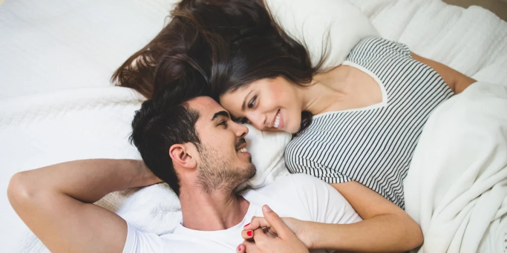 A smiling couple lies on a bed, looking into each other's eyes, conveying connection and the benefit of "best condoms."